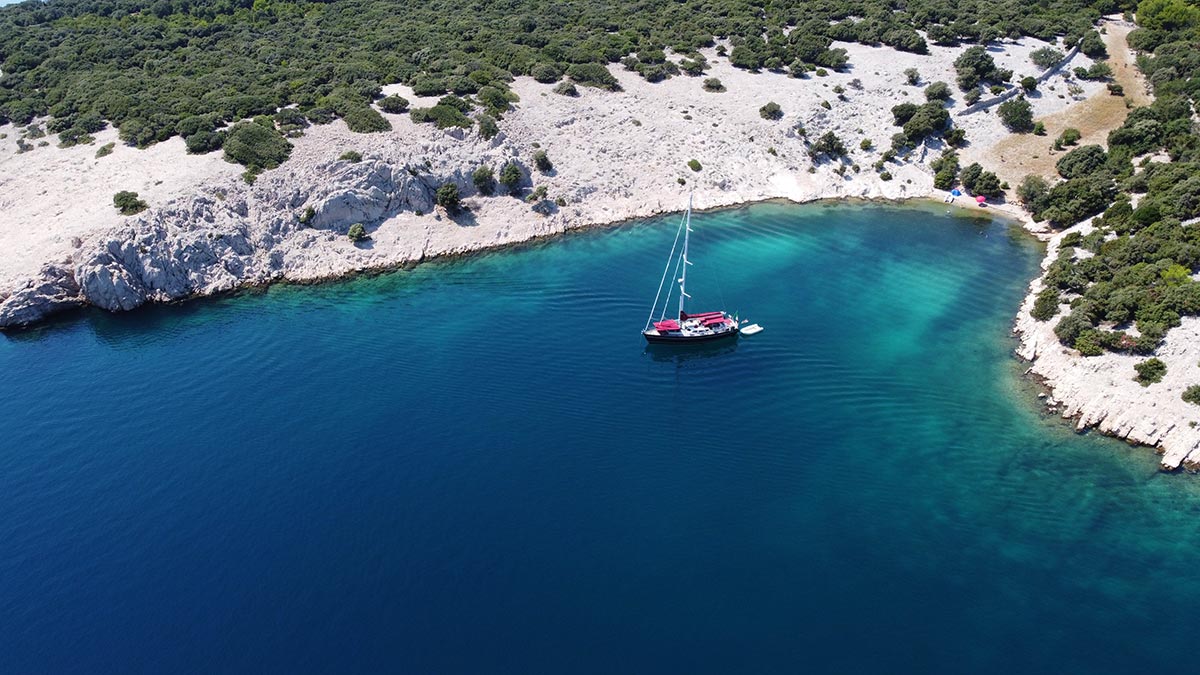 Small beach and anchored sailboat in the blue waters of Šimuni bay on Pag Island